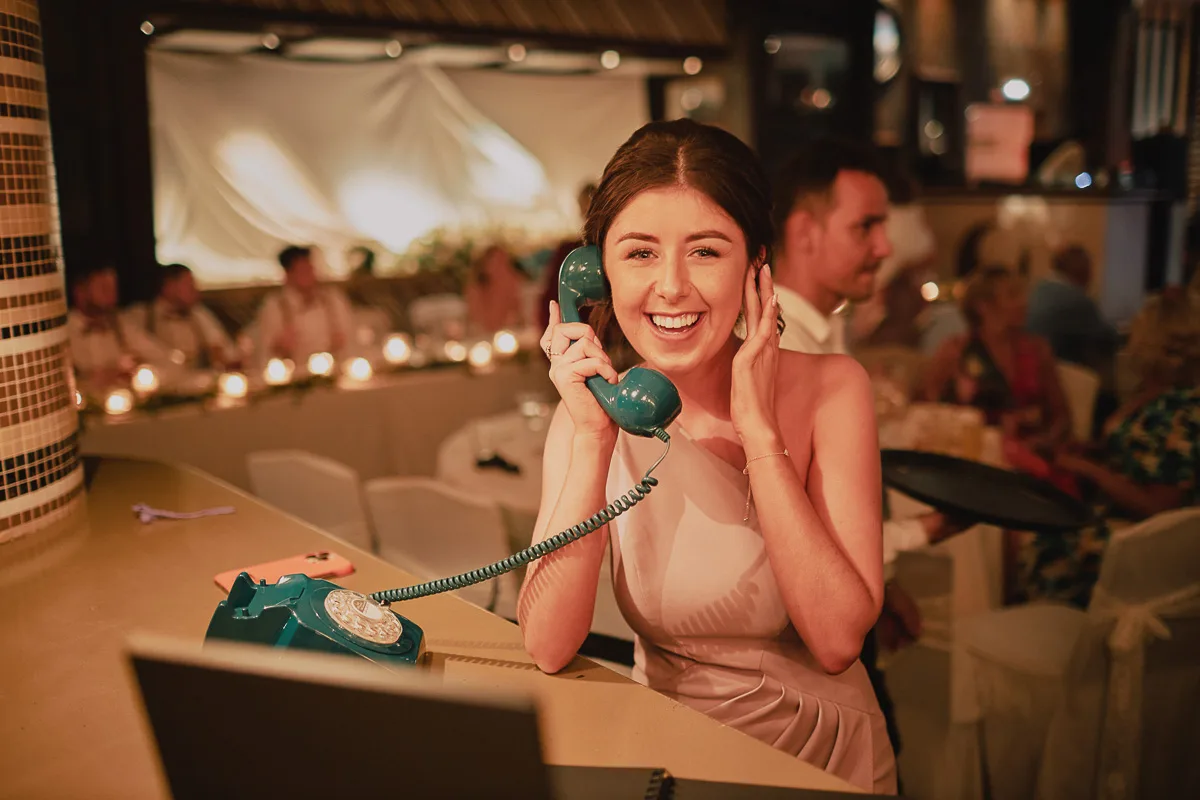 A wedding guest leaving a message on a teal Loveline phone at a reception